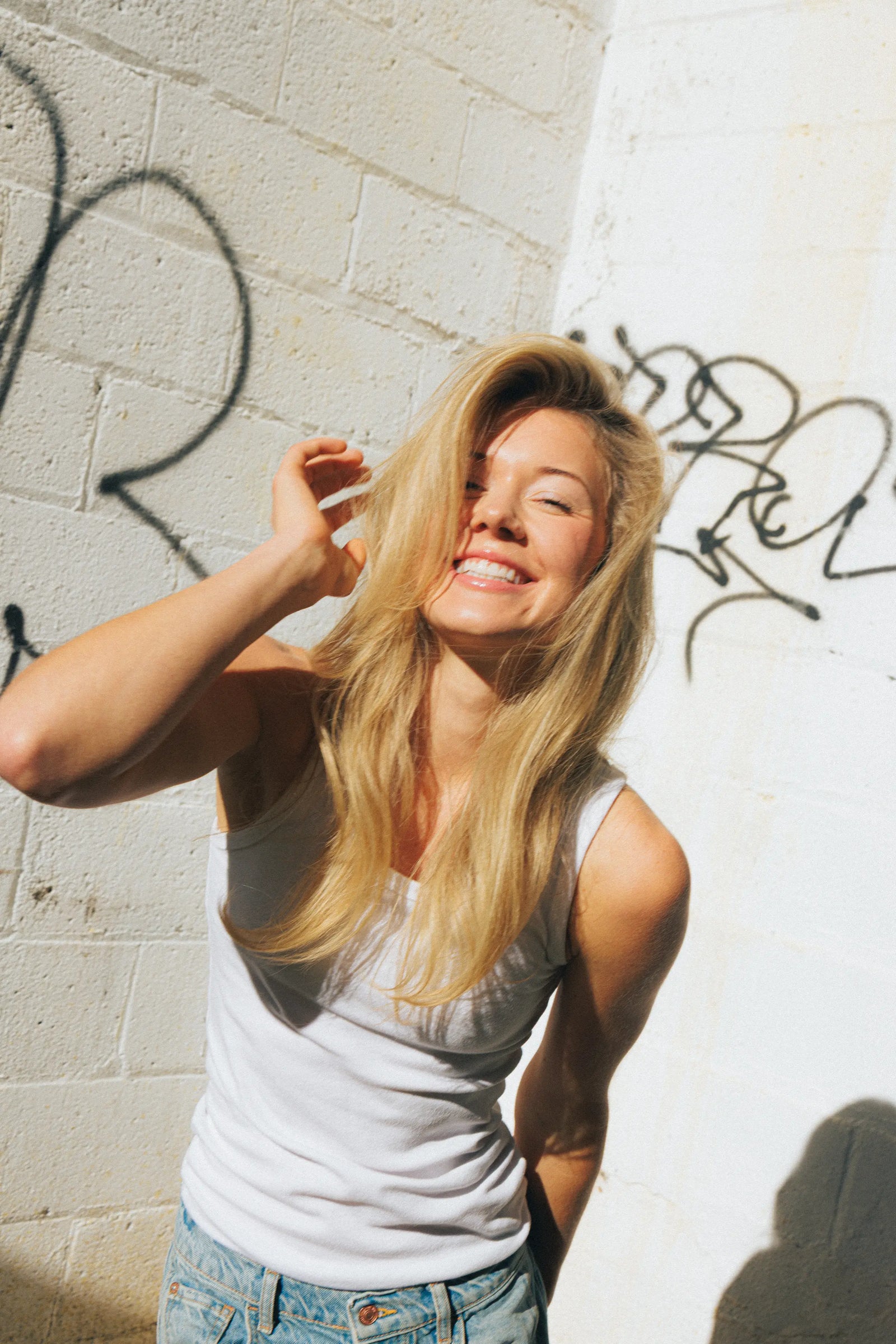 Thickening hair treatment results on a smiling woman with long, flowing blonde hair leaning against a graffiti wall in sunlight.