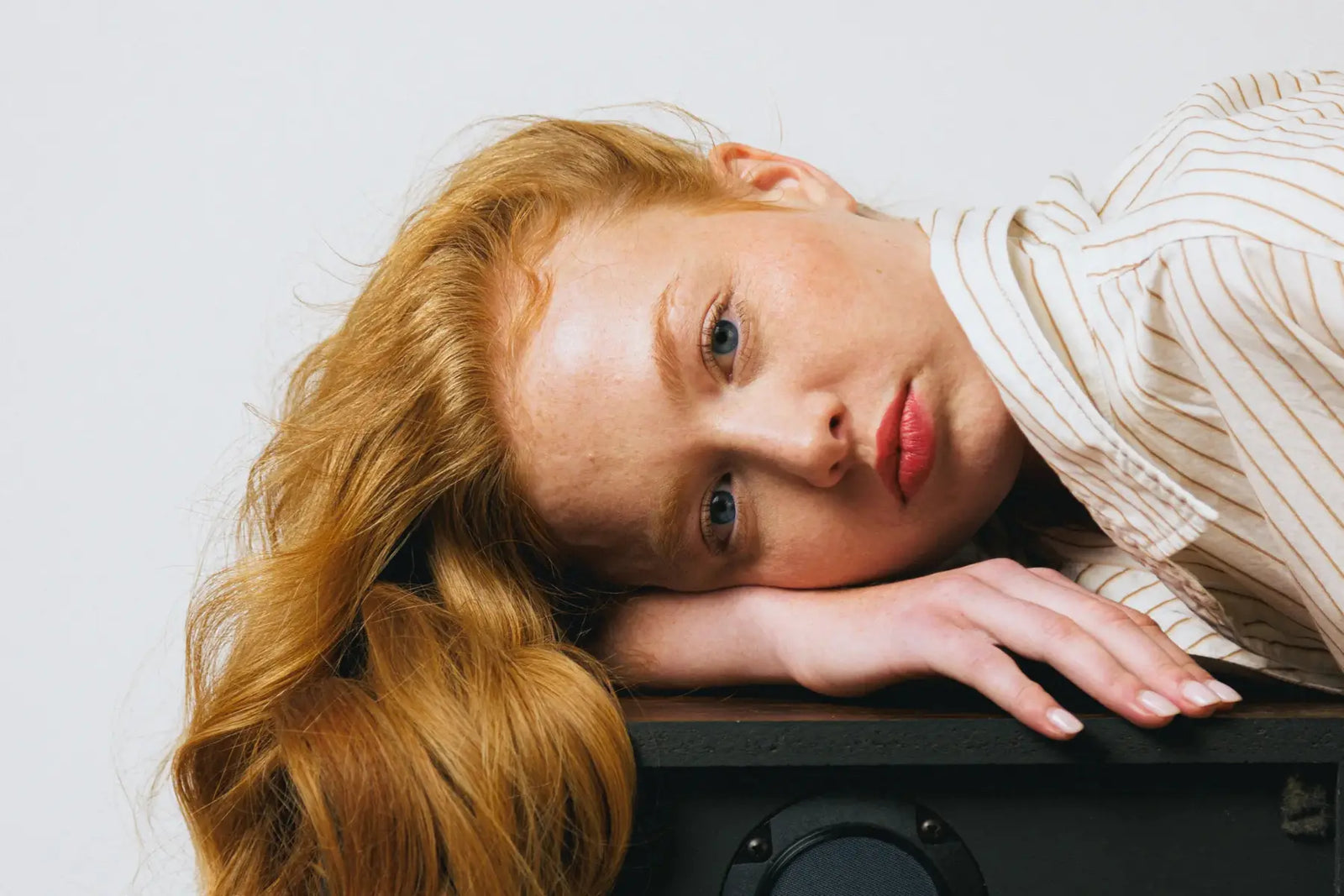 Volumizing hair treatment results displayed on a redhead with long, voluminous copper waves resting against a black speaker.