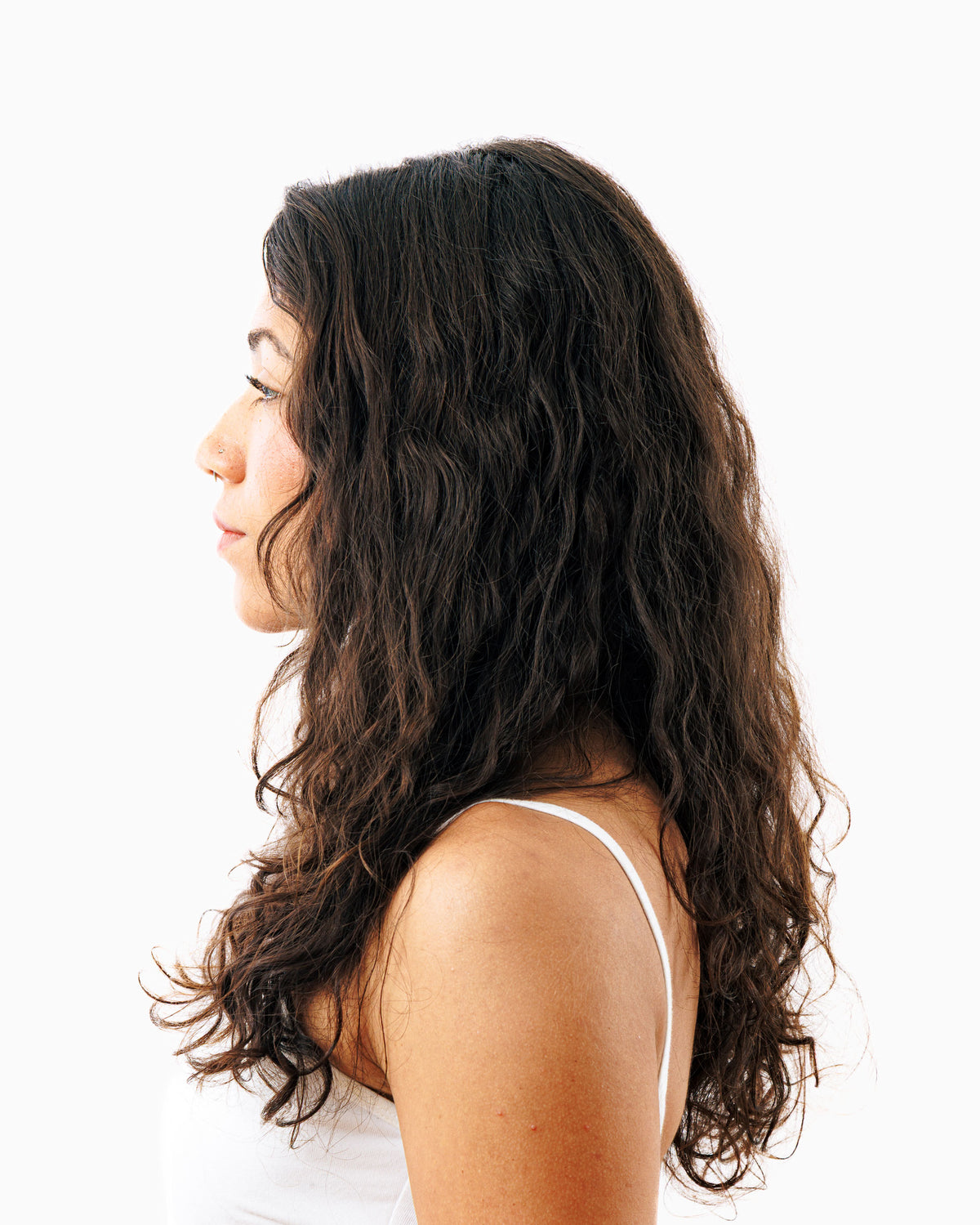 Side profile of woman with thick, voluminous wavy dark hair showcasing results of Decibel thickening hair products.