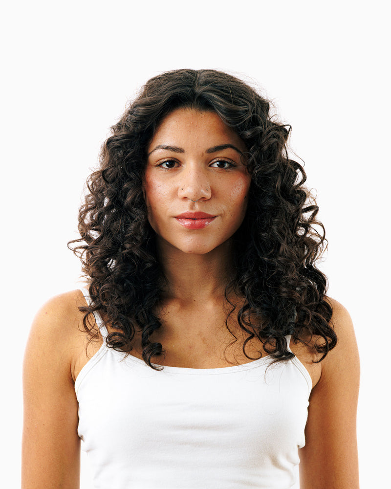 Woman with full, defined curly hair showcasing volumizing results from Decibel thickening hair care.