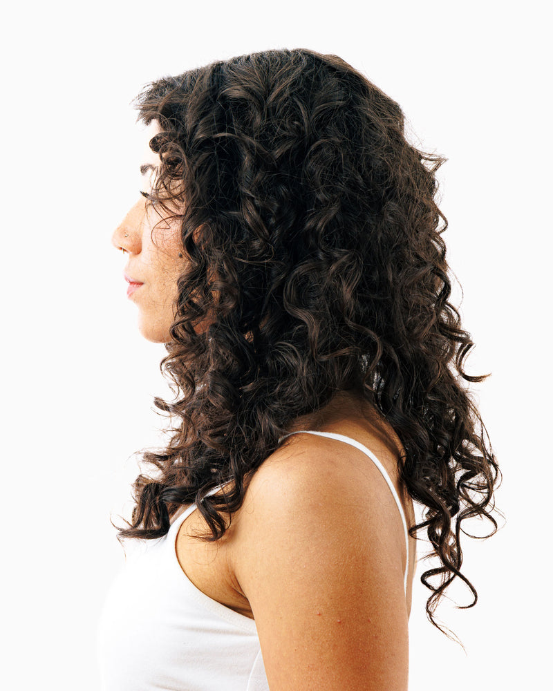 Side profile showing voluminous dark curly hair after using thickening shampoo for fuller body.