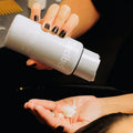 Stylist dispensing Decibel thickening conditioner into a client's palm at a salon wash station.