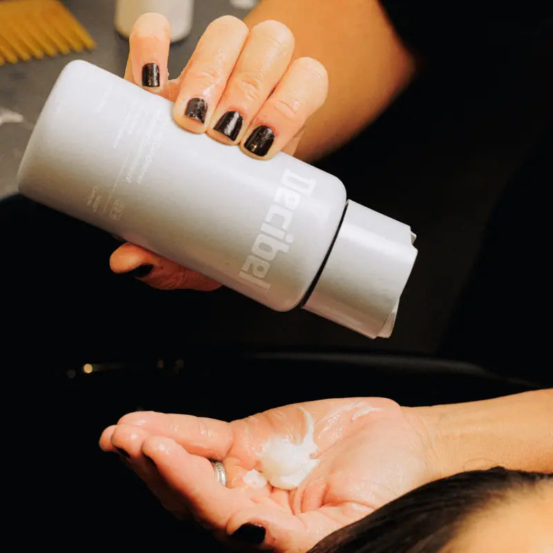 Stylist dispensing Decibel thickening conditioner into a client's palm at a salon wash station.