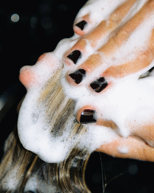 Close-up of hands massaging Decibel thickening shampoo lather through wet hair.