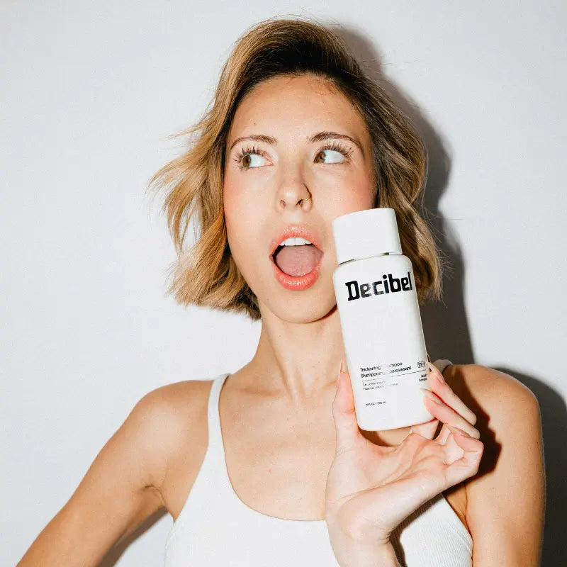 Woman with voluminous short blonde hair holding Decibel Thickening Shampoo with an excited expression.